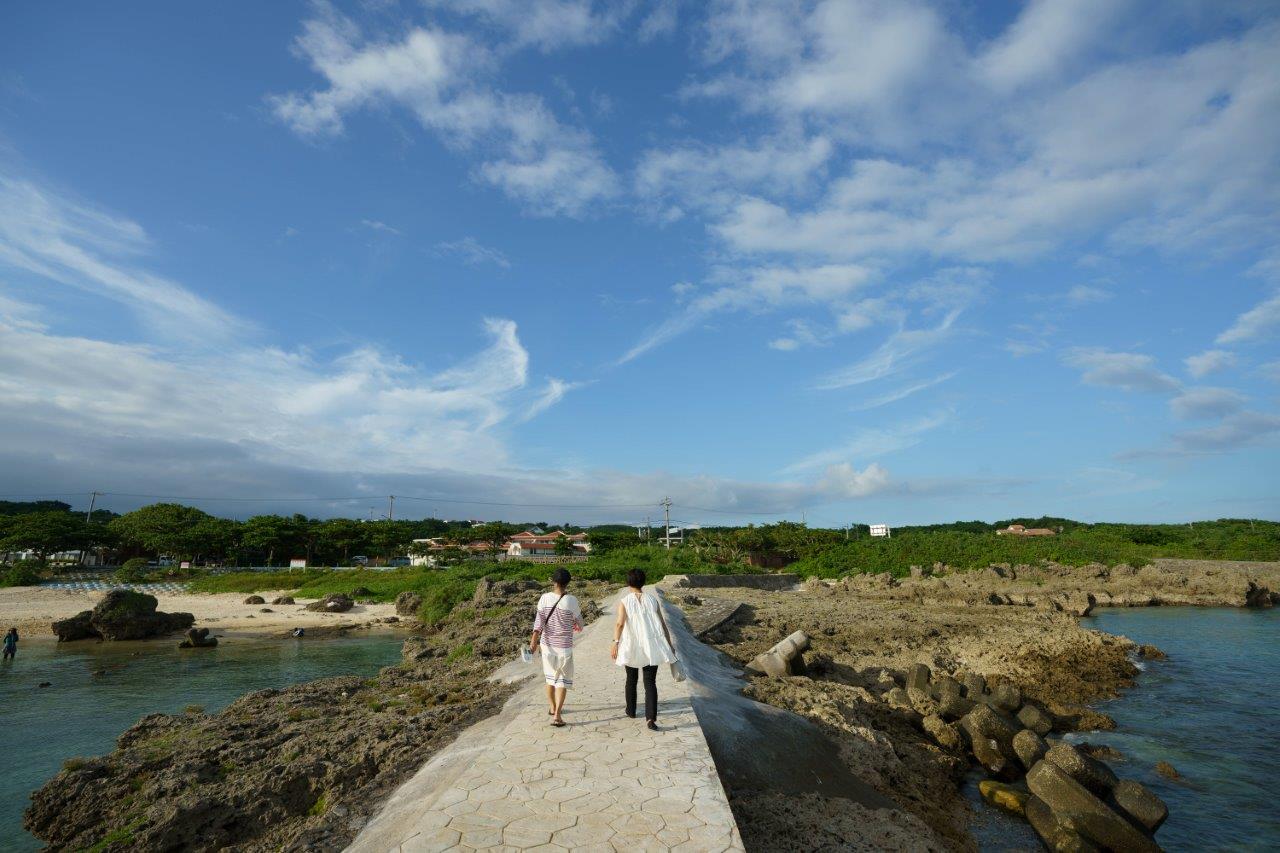 海沿いの道をあるくタサン志麻さんとツアーガイド